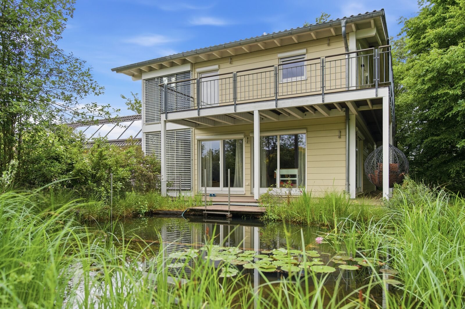 Rückansicht des Hauses mit Balkon und Teich bei Tag